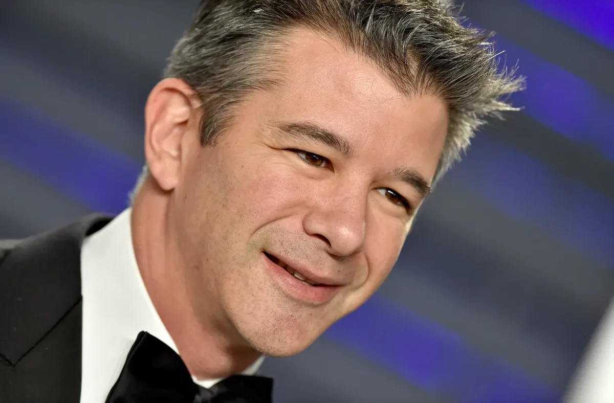 Travis Kalanick, former Uber CEO, discussing the future of industrial robotics and AI with a backdrop of automated factory machinery.