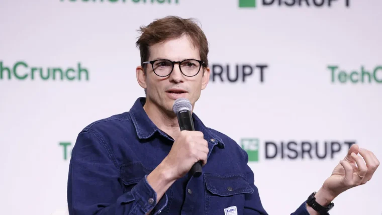 Ashton Kutcher and Morgan Beller shaking hands, with a background illustrating AI infrastructure elements like server racks and energy symbols.