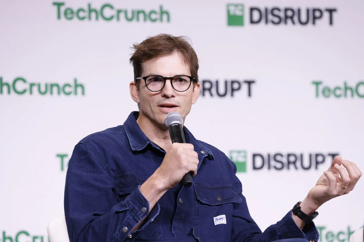 Ashton Kutcher and Morgan Beller shaking hands, with a background illustrating AI infrastructure elements like server racks and energy symbols.