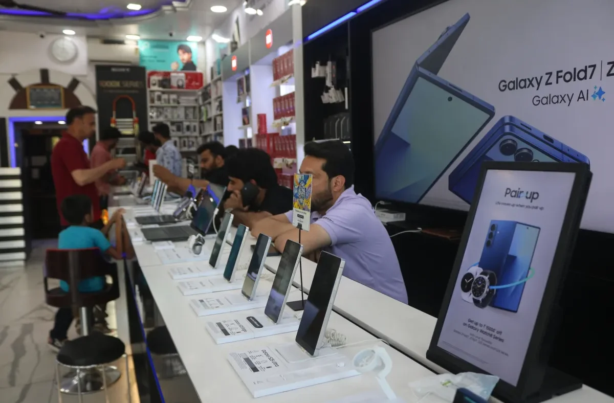 Workers assembling smartphones in an Indian factory with visible memory chips on circuit boards, illustrating the impact of AI demand on component pricing.
