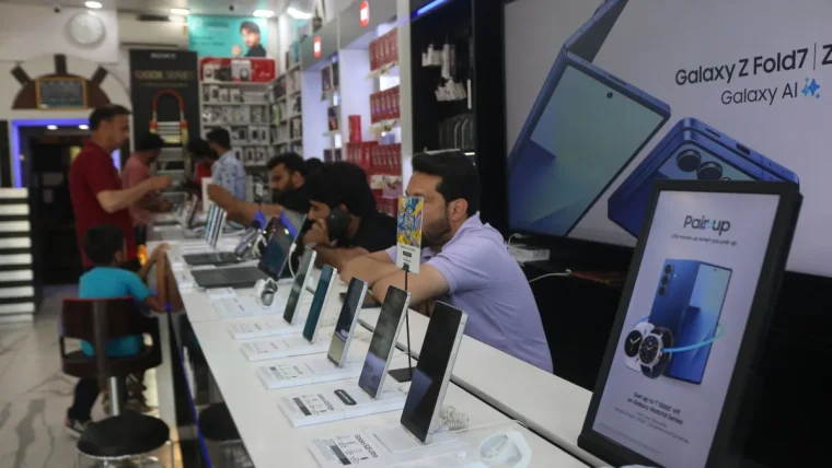 Workers assembling smartphones in an Indian factory with visible memory chips on circuit boards, illustrating the impact of AI demand on component pricing.