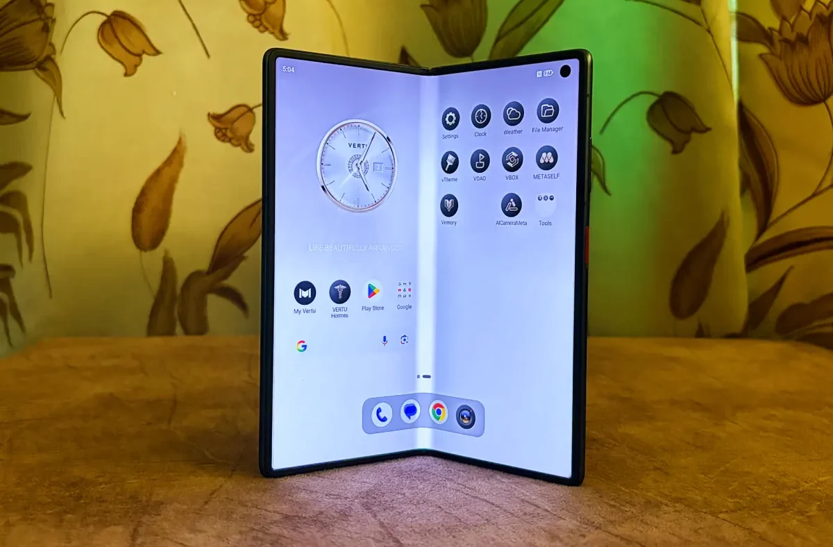 A Vertu Alphafold luxury foldable smartphone open, displaying its screen with an AI agent interface, next to executive-style accessories.