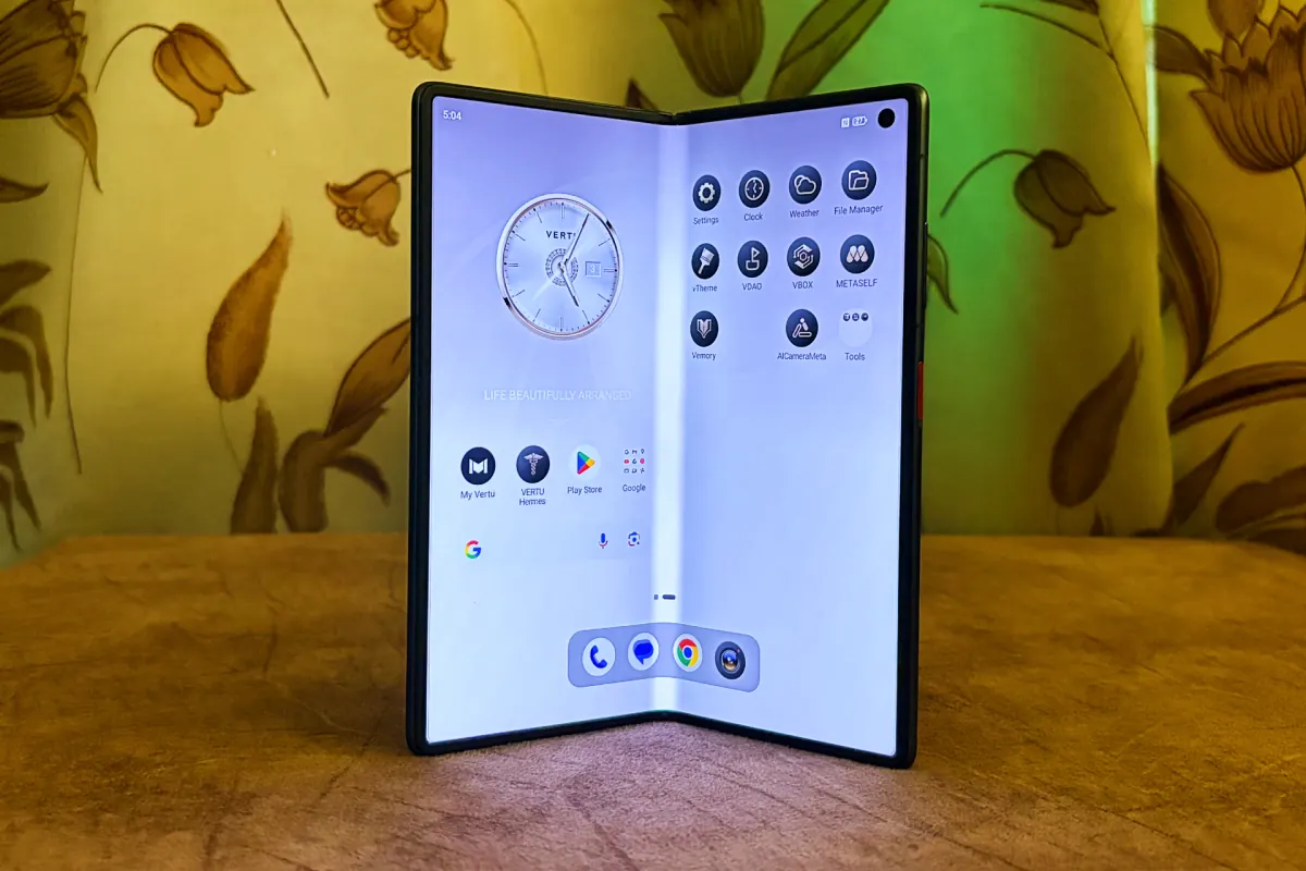 A Vertu Alphafold luxury foldable smartphone open, displaying its screen with an AI agent interface, next to executive-style accessories.
