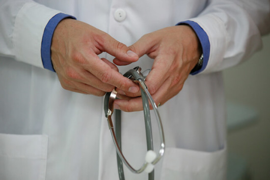 NMC guidelines document and stethoscope on a desk next to a laptop showing a medical advertisement with an AI-generated content label